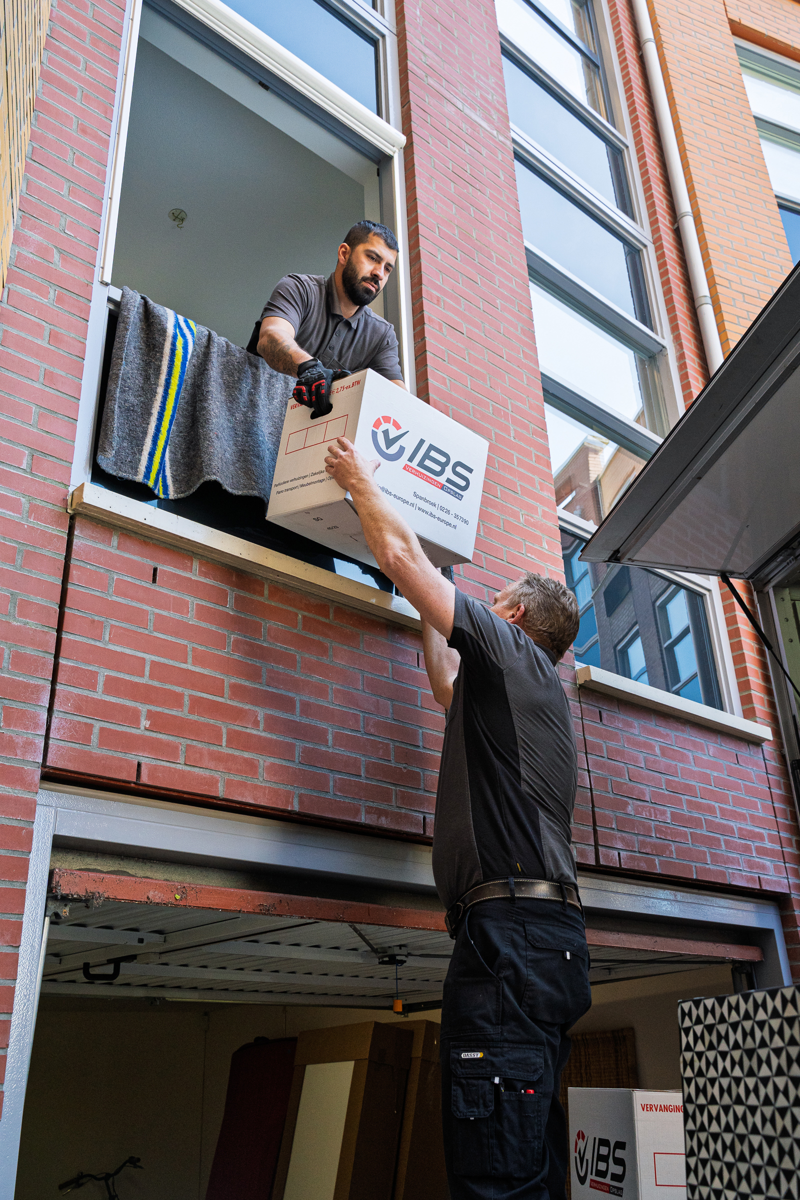 Verhuizers geven een verhuisdoos via een raam naar binnen
