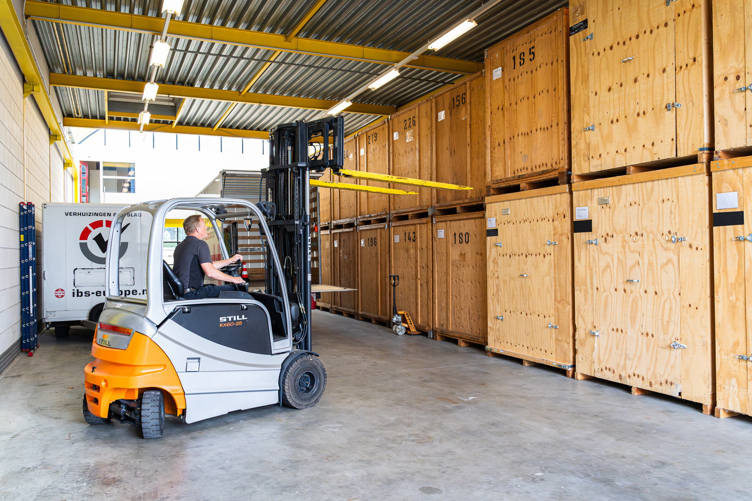 Medewerker van IBS rijdt met een heftruck tussen houten opslagcontainers