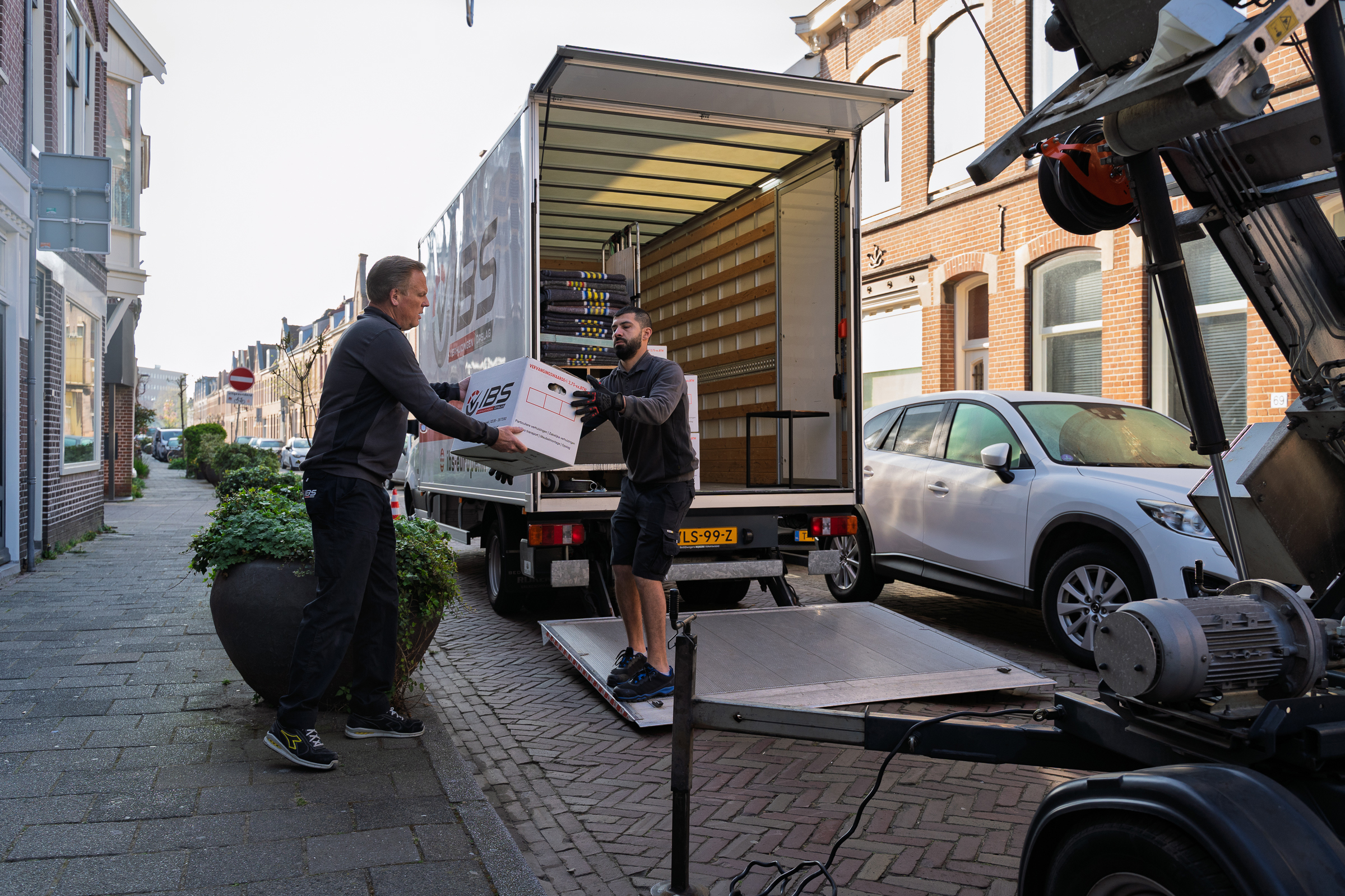 Verhuizers van IBS laden verhuisdozen uit een verhuiswagen